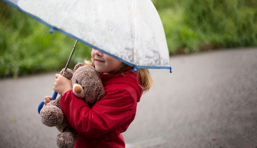 Child with a teddy under an umbrella